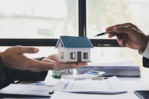 Real estate agent home sales broker holding calculator and pointing to the house model and explains the business contract