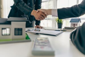 A real estate agent shakes hands with a client after completing a transaction regarding a house contract agreement
