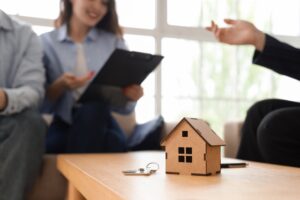 House figure and key on table against couple signing agreement with real estate agent in room
